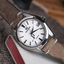 Load image into Gallery viewer, A watch with a grey stonewash suede band and a silver-colored case, placed on a textured surface.